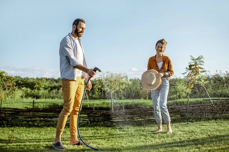 Young man and woman watering green lawn, taking care of the beautiful backyard in the countrysideの写真素材