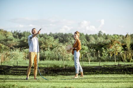 Young man and woman watering green lawn, taking care of the beautiful backyard in the countrysideの写真素材
