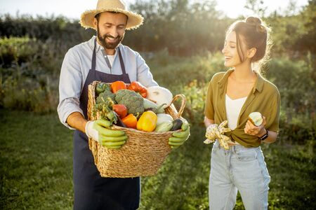 Portrait of a man and woman holding basket full of freshly picked up homegrown vegetables at the countryside on a sunny eveningの写真素材