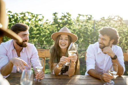 Group of a young people drinking wine and having fun together while sitting at the dining table outdoors on the vineyard on a sunny eveningの写真素材