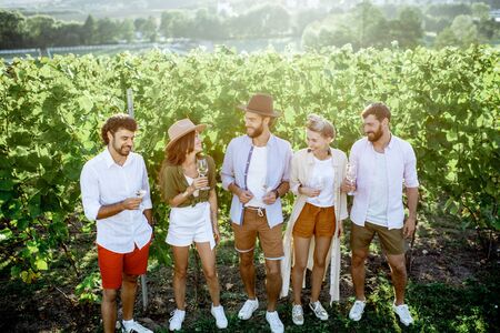 Group of young friends dressed casually hanging out together, tasting wine on the vineyard on a sunny summer morningの写真素材