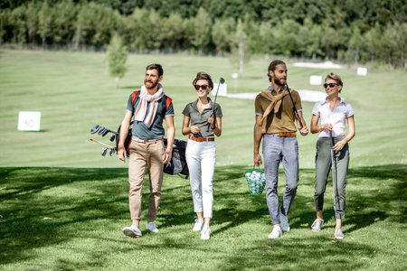 Young and elegant friends walking with golf equipment, hanging out together before the golf play on the beautiful course on a sunny dayの写真素材