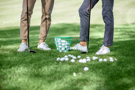Friends standing together with golf equipment and balls on the green grass, cropped image with no...