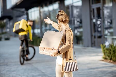 Misguided woman calling back a courier that ride away on the background, deliveryman fooling a customer with bad pizzaの写真素材
