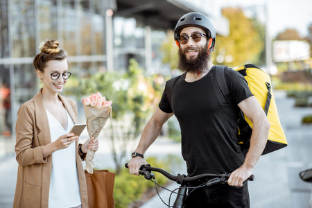 Courier delivering fresh flowers to a young business woman on a bicycle wearing delivery backpack....