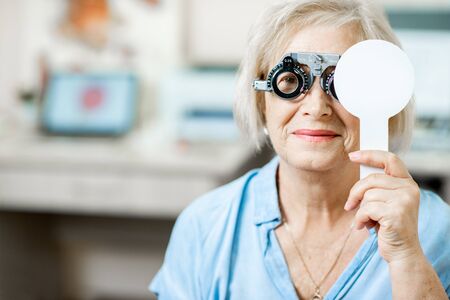 Senior woman checking vision with eye test glasses and scapula during a medical examination at the ophthalmological officeの写真素材