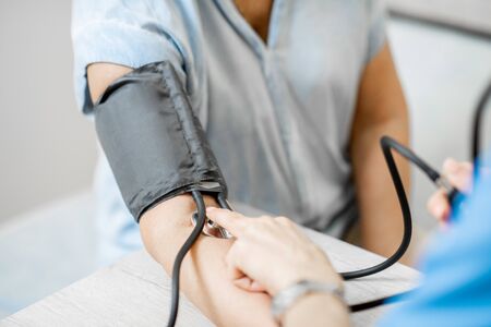 Nurse measuring blood pressure of a senior woman patient during an examination in the clinic, close-up view with no faceの写真素材