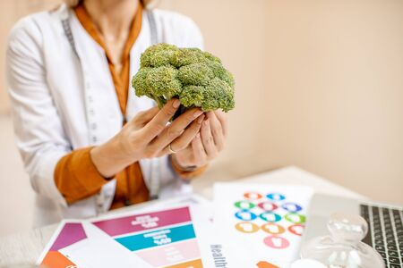 Nutritionist holding fresh broccoli, working on a diet plan in the officeの写真素材