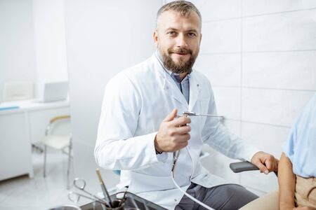 Portrait of a senior otolaryngologist in medical gown with ENT flushing tool in the procedure roomの写真素材