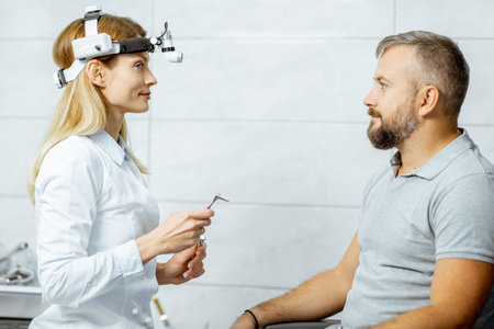 Otolaryngologist preparing for the medical examination procedure to an adult man, holding larynx...