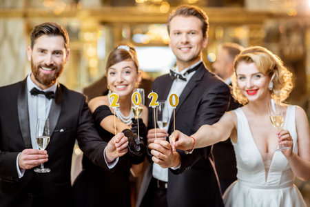 Portrait of an elegantly dressed people holding candles with 2020 numbers, celebrating New Year holiday at the luxury classical restaurant hallの写真素材