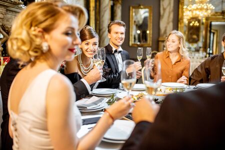 Elegantly dressed group of people having a festive dinner at a well-served table near the christmas tree, celebrating New Year holiday at the luxury restaurantの写真素材