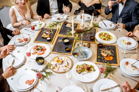 People having a festive dinner at a well-served table with tasty dishes during New Year Eve at the luxury restaurantの写真素材