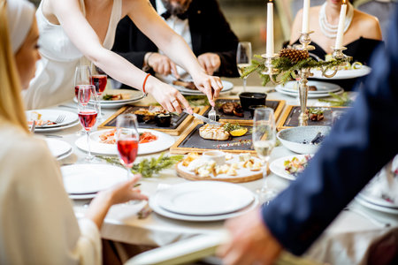 People having a festive dinner at a well-served table with tasty dishes during New Year Eve at the luxury restaurant, close-up view with no faceの写真素材