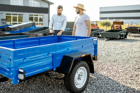 Agronomist with salesman choosing a new farm truck trailer, standing on the open ground of the...