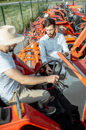 Young agronomist with elegant salesman choosing a tractor for farming on the open ground of...