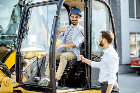 Builder choosing heavy machinery for construction with a sales consultant on the open ground of a shop with special vehiclesの写真素材