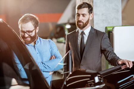 Sales consultant showing to the client vehicle intreior at the car dealership. Concept of selling eco-friendly and modern carsの写真素材