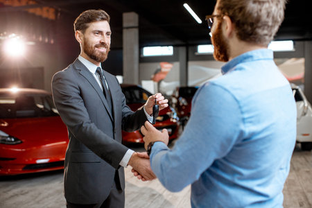 Sales consultant handing car keys to the client at the car dealership. Concept of buying eco-friendly and modern carsの写真素材