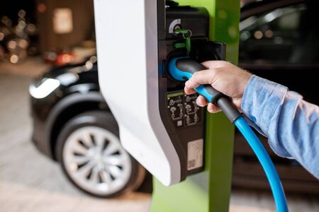 Man plugging cable into the charging station for electric cars at the car dealership, close-up viewの写真素材