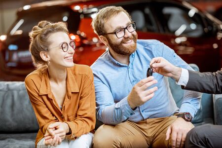 Young and happy couple sitting together on the comfortable couch, buying a new car at the dealershipの写真素材