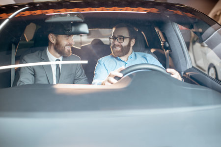 Sales manager with a young client inspecting vehicle interior at the car dealership, view through...