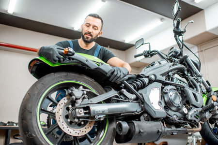 Handsome worker in overalls mounting motorcycle wing after a repairment in the workshop. Concept of...