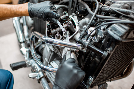 Worker in protective gloves adjusting engine valves of a beautiful vintage motorcycle at the...