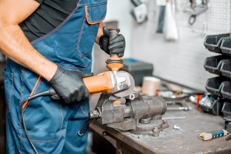 Handyman in overalls cutting metal tube with electric grinder mastering or repairing something in...