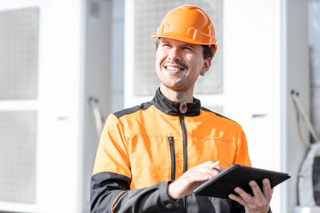Portrait of a professional workman in protective clothing adjusting the outdoor unit of the air...
