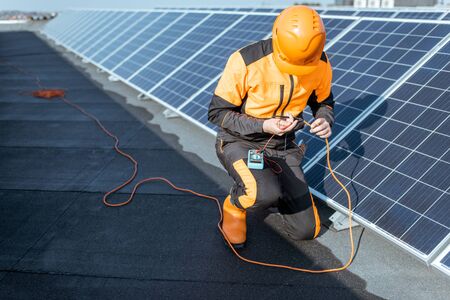 Well-equipped electrician connecting solar panels, checking the voltage and connecting wiring on a rooftop photovoltaic power plantの写真素材