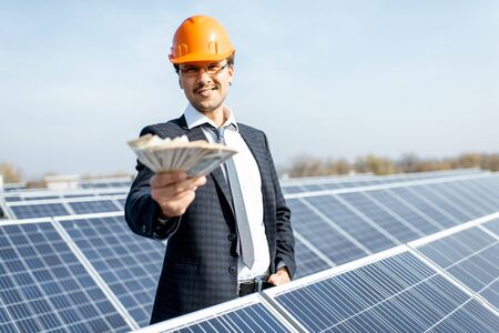 Portrait of a happy businessman with money earned from the electricity production of a solar station. Concept of successful investment in alternative energyの写真素材