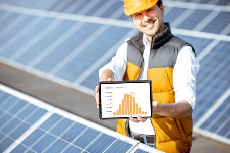 Man showing genaration of solar power plant, holding digital tablet with a chart of electricity production. Concept of online monitoring of the electric stationの写真素材