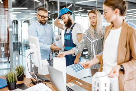 Group of engineers and workman working on a project of alternative energy at the office with computer, wind turbine and solar panels modelの写真素材