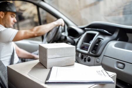 Delivery man driving cargo vehicle with parcels on the passenger seat, image focused on the cardboard boxes with blank spaceの写真素材
