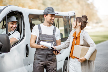 Delivery company employees in uniform delivering goods to a client by cargo van vehicle, woman...