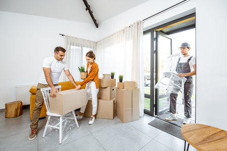 Young couple in the living room of their new home, mover performs professional furniture delivery...