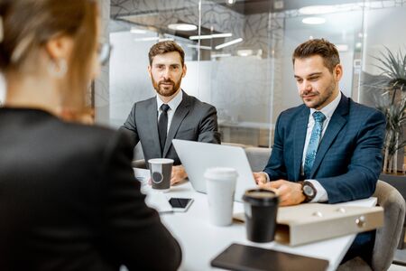 Business men stricly dressed in the suits sitting during a conference with employees in the meeting roomの写真素材