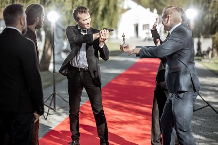 Group of a men as a well-known movie actors and secret agent playing with handgun during awards ceremony on the red carpet outdoorsの写真素材
