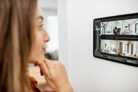Young woman watching video from security cameras on a digital tablet at home. Concept of remote video surveillance over the internet with smart devicesの写真素材