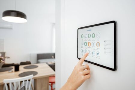 Controlling home with a digital touch screen panel installed on the wall. Close-up on a screen with mobile application for managing smart devicesの写真素材