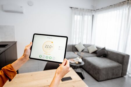 Controlling home heating temperature with a digital tablet. Concept of a smart home and mobile application for managing smart devices at homeの写真素材