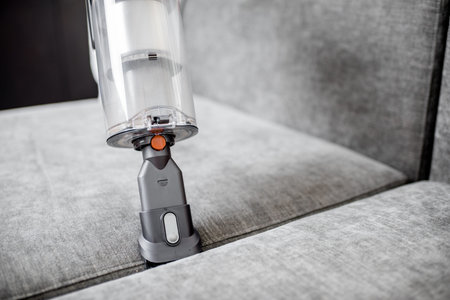 Woman cleaning sofa with a modern cordless vacuum cleaner with a special nozzle, close-up. Dry cleaning concept with wireless vacuum cleanerの写真素材