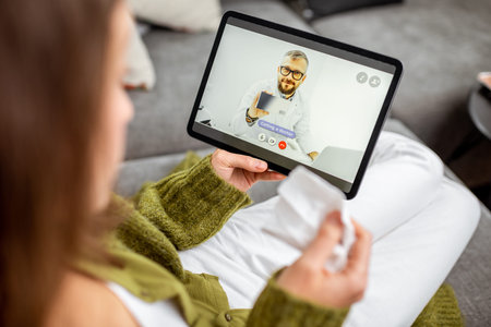 Woman talking with a doctor online using digital tablet, feeling bad at home. Concept of...