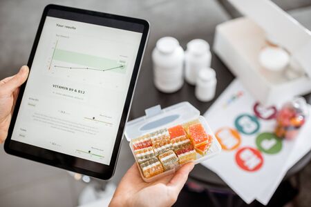 Woman checking the result of medical tests on a digital tablet, close-up with nutritional supplements on the background. Concept of individual online selection of food supplementsの写真素材