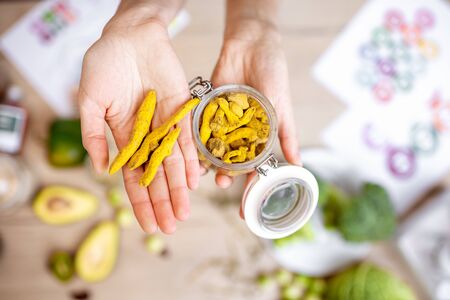 Holding turmeric root at the table with healthy vegan food ingredients and supplements, top view. Concept of curcuma as a new trend in food and cosmetic industryの写真素材