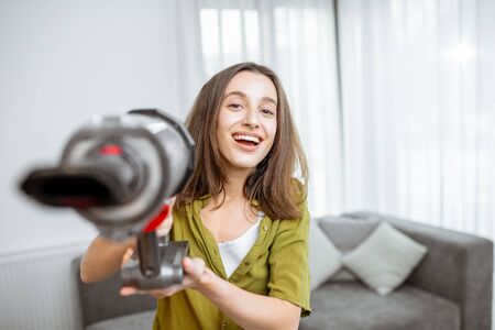 Portrait of a young and happy woman with cordless vacuum cleaner, enjoying housework at home. Concept of an easy cleaning with wireless toolsの写真素材