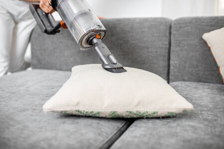 Woman cleaning sofa with a modern cordless vacuum cleaner with a special nozzle, close-up. Dry cleaning concept with wireless vacuum cleanerの写真素材