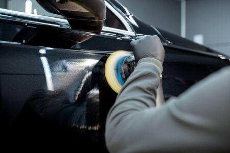 Car service worker polishing vehicle body with special wax from scratches, close-up. Professional car detailing and maintenance conceptの写真素材