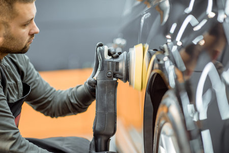 Worker polishing vehicle body with special grinder and wax from scratches at the car service...